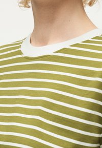 Κοντινή λήψη λαιμού και άνω στήθους με πράσινο και άσπρο ριγέ πουκάμισο και λευκή στρογγυλή λαιμόκοψη.