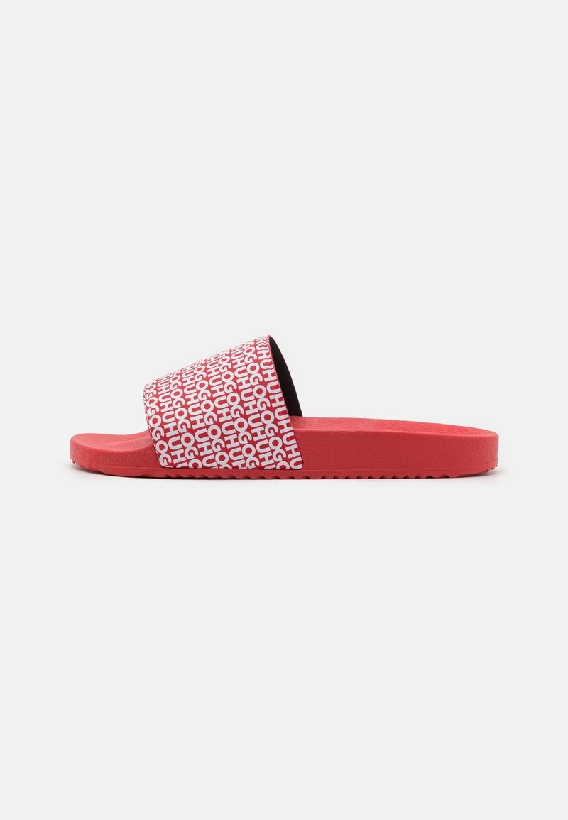 Sandale slide rouge avec un motif de texte blanc répétitif sur la bride, sur un fond clair uni, vue de côté.