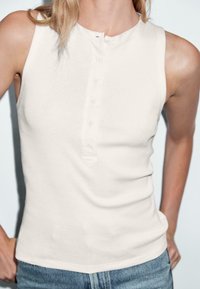 Světlý béžový bezrukávový tank top v henley stylu, s knoflíkovou légu a měkkou, hladkou bavlněnou tkaninou.
