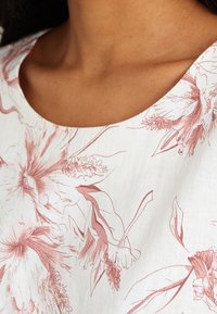 Blumenbluse mit weißem Hintergrund und rosa floralen Mustern, einem runden Ausschnitt und einem strukturierten Stoff.
