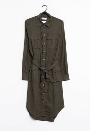 Olivově zelené šaty-košile s dlouhým rukávem, zapínáním na knoflíky vpředu, dvěma kapsami na prsou, dvěma spodními kapsami, límcem a pásem v pase, zavěšené na černém ramínku.
