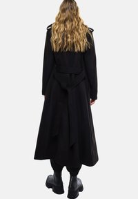 Lange zwarte jas met een strik taille, gemaakt van een zacht materiaal, met een lange silhouet en een minimalistisch ontwerp.