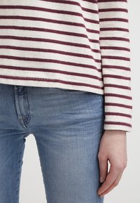 Haut rayé marron et crème avec une texture douce, associé à un jean denim bleu clair. Comporte des manches longues et une coupe décontractée.