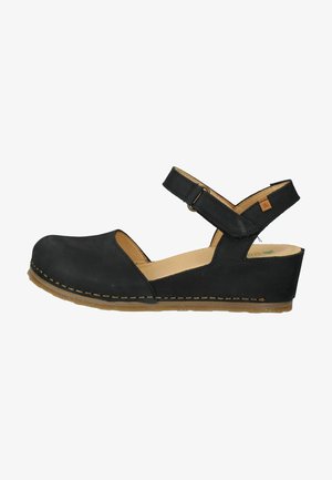 Zwarte wig-sandalen met een verstelbare band, open teen en zachthuid materiaal. Gestikte details langs de zool en een voetenbed met een natuurlijk houten effect.