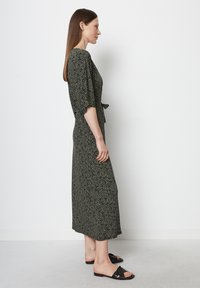 Robe midi à motifs noir et blanc avec des manches courtes bouffantes, dotée d'un nœud à la taille. Associée à des sandales plates noires.