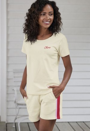 Light yellow cotton t-shirt with "Chérie" embroidered in red. Paired with matching shorts featuring red and pink side stripes. Casual fit.