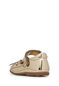 Zlaté lakované boty s kulatou špičkou, nastavitelným páskem a dekorační mašlí na přední straně. Hladký povrch s gumovou podrážkou.