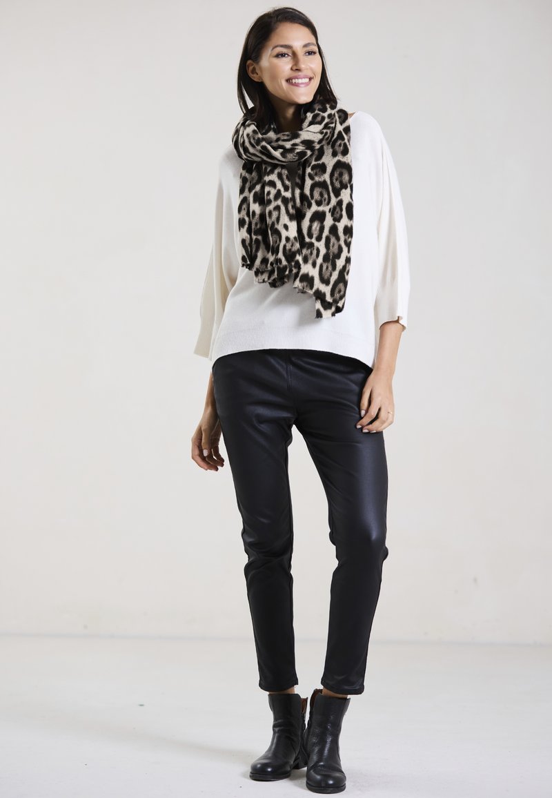 White knit sweater, black faux leather pants, and a beige leopard-print scarf. Black ankle boots complete the outfit. Simple background.