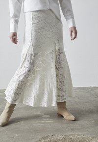 Hvid blonde maxi-nederdel med blomsterprint, flagrende kant, sideslids, lagdelt design, parret med beige ankelstøvler. Struktureret stof.