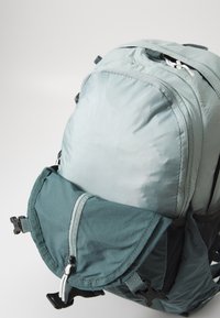 Ryggsäck i en ljusgrå och grön färgsättning; har en dragkedjefrontficka, justerbara remmar och en strukturerad tygfinish.