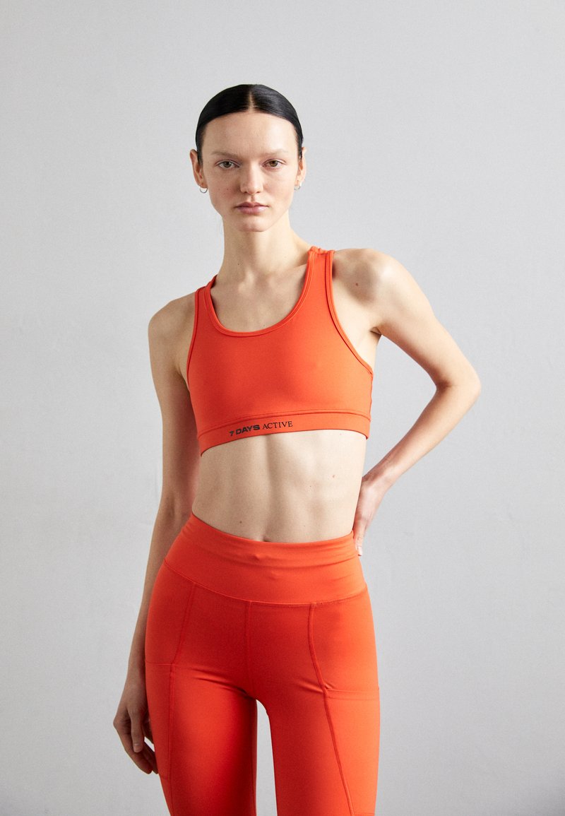 Orange athletic crop top and matching high-waisted leggings, made of smooth, stretchy material. Features a logo band on the top.