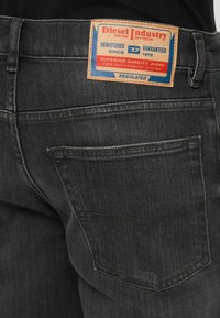 Mustad teksad nahast märgiga, millel on "Diesel Industry" bränding. Disain hõlmab tagataskut ja nähtavaid õmbluse detaile.