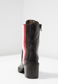 Bottine en cuir noir avec une bande rouge et blanche sur le côté, talon carré, fermeture éclair et doublure intérieure en tissu rayé.