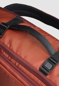 Bolsa de deporte de tela marrón con superficie texturizada, con una correa negra, hebilla de plástico y una cremallera a lo largo de un lado.