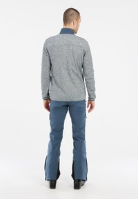 Grijze textuur fleece pullover met een hoge kraag, gecombineerd met blauwe waterdichte skibroek met ritsen aan de zijkanten en zwarte accenten.