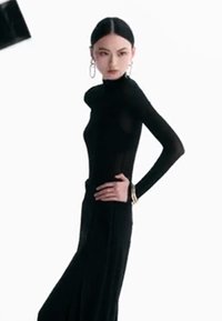 Vestido negro de manga larga hecho de material transparente, con un diseño ajustado, cuello alto y acentos de pulsera dorada.