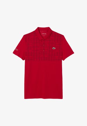 Polo rosso realizzato in tessuto morbido, con un motivo geometrico in rosso scuro, colletto con chiusura a due bottoni e logo Lacoste sul petto.