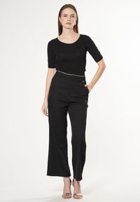 Top corto nero a maniche corte con finituraTexture, abbinato a pantaloni larghi neri a vita alta. Dettagli in argento in vita e nelle scarpe.