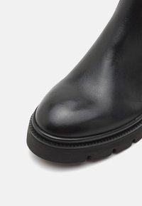 Juodas odinis kulkšninis botas su apvaliu galiuku, tekstūruotu paviršiumi ir storu guminio pado, kuriame yra griovelių raštas.