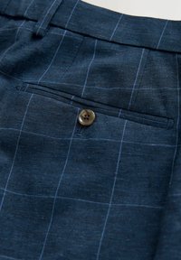 Navy-blaue Stoffhose mit einem dezenten Karomuster, strukturierten Oberfläche und einer einzelnen Tasche mit einem braunen Knopfverschluss.