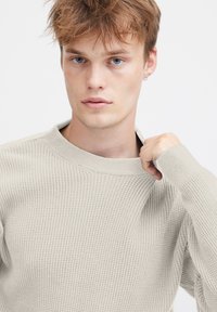 Beige gerippter Strickpullover mit Rundhalsausschnitt und langen Ärmeln. Hat ein strukturiertes Muster und eine leicht entspannte Passform.