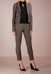 Skräddarsydd grå blazer och matchande figurnära byxor, textil med en lätt struktur. Svart blus under och svarta högklackade skor.