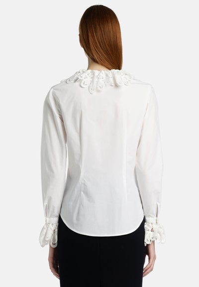Weiße Bluse mit einem Kragen aus Spitze und Spitzendetails an den Ärmelabschlüssen. Hergestellt aus glattem Stoff, hat sie eine taillierte Passform und einen geschwungenen Saum.