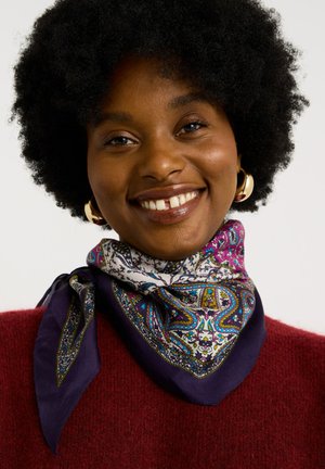 Bufanda de seda multicolor con un intrincado patrón de paisley, que presenta tonos de morado, azul y blanco, atada alrededor del cuello.