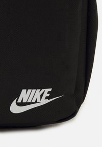 Tessuto nero con texture, logo Nike bianco e swoosh nell'angolo inferiore di una borsa o pochette.
