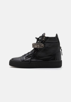 Sapatilhas altas pretas feitas de couro, com fechos de zipper, cordões e uma fita decorativa com detalhes em relevo. Sola em borracha.