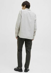 Cămașă rayată, de culoare deschisă, cu un croi lejer, asociată cu pantaloni verzi închis și pantofi negri, evidențiind un design minimalistic și contrastant.