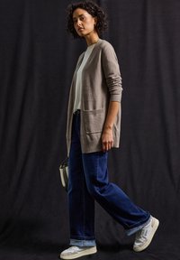 Ljusgrå cardigan med fickor, bärs över en vit topp och blå vida jeans. Modellen har på sig gråa och vita sneakers och bär en liten väska.