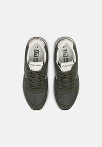 Dark green sneakers with lace-up design, padded collar, and cushioned insole. Features a white logo and textured rubber sole.