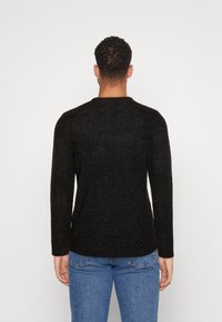 Schwarzer gestrickter Pullover mit langen Ärmeln und rundem Ausschnitt, mit einem strukturierten Muster. Mit blauen Jeans kombiniert.
