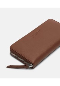 Brązowy portfel ze skóry o fakturowanej powierzchni, z zamkiem błyskawicznym i paskiem na nadgarstek. Na przedniej stronie znajduje się wytłaczane logo.