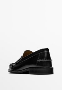 Black leather loafers with a smooth finish, low heel, rounded toe, and a decorative stitched detail at the back.