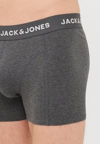 Graue Baumwoll-Boxershorts mit einem schwarzen elastischen Bund, auf dem der Text „JACK & JONES“ in Weiß zu sehen ist. Der Stoff hat eine glatte Textur.