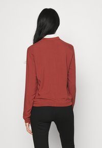 Pull-over à manches longues de couleur rouille, confectionné dans un tissu doux, avec un col rond et une coupe ajustée, dos uni.