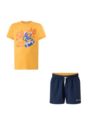 T-shirt gialla a maniche corte con grafica e testo sullo skateboard, abbinata a pantaloncini blu navy con coulisse e piccolo logo bianco.