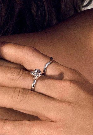 Sølv ringe på en hånd med et snoet design og en knyttet detalje. Ringene har en poleret overflade og en glat tekstur.