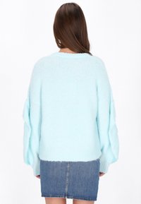 Jasnoniebieski oversize sweter z miękkiego, puszystego materiału, z prążkowanym dołem i szerokimi rękawami, w zestawie z dżinsową mini spódnicą.