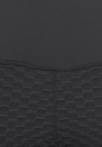 Schwarzer Sportstoff mit einem glatten oberen Bereich und einem strukturierten unteren Bereich, der ein hexagonales Muster aufweist. Sichtbare Nahtdetails.