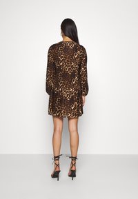 Vestito tigrato con maniche lunghe e dettagli a pieghe, nelle tonalità di marrone e nero. Abbinato a scarpe con tacco alto nere e con cinturini.