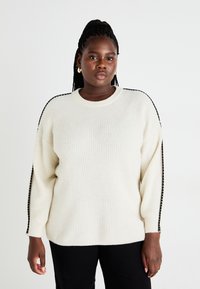 Κρέμα-χρωμα προς το πλέκτο πουλόβερ με ριγωτή υφή, που διαθέτει μαύρες λεπτομέρειες στους ώμους και ελεύθερη εφαρμογή.