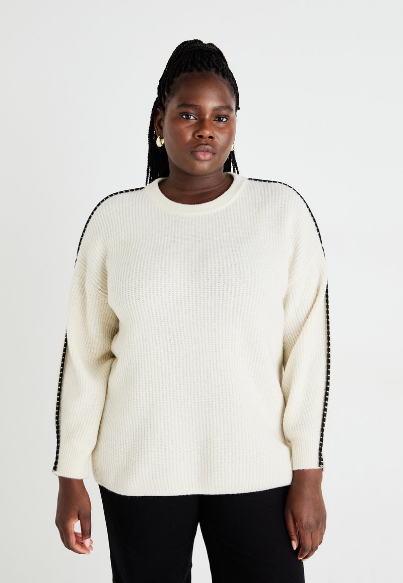 Κρέμα-χρωμα προς το πλέκτο πουλόβερ με ριγωτή υφή, που διαθέτει μαύρες λεπτομέρειες στους ώμους και ελεύθερη εφαρμογή.