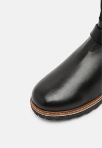 Schwarzer Lederstiefel mit glänzendem Finish, rund zulaufender Spitze und kontrastierenden braunen Nähten an der Sohle. Robuste Gummisohle für guten Halt.