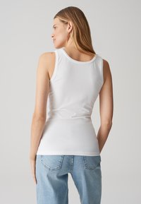 Débardeur blanc en matériau doux et extensible. Présente un col rond et une coupe ajustée, associé à un jean en denim bleu clair.
