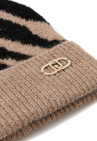 Beanie a maglia in tonalità beige con strisce nere, con un logo in accentuazione dorata sull'orlo ripiegato. Tessuto morbido e testurizzato con design a coste.