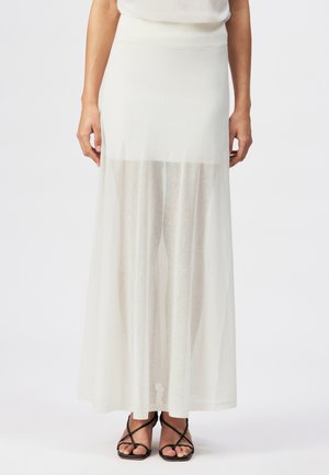 Weißer Maxirock mit transparentem Überwurf, der darunter liegende Spitzen-Shorts zeigt, getragen mit schwarzen, Riemchen-Open-Toe-Absätzen.