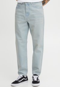 Vaqueros de denim azul claro con un diseño de pierna recta, estilo clásico de cinco bolsillos y un lavado desgastado. Llevados con zapatillas negras.